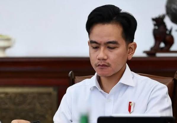 Gibran Rakabuming Raka mengenakan kemeja putih saat mengikuti kegiatan di sebuah ruangan resmi.