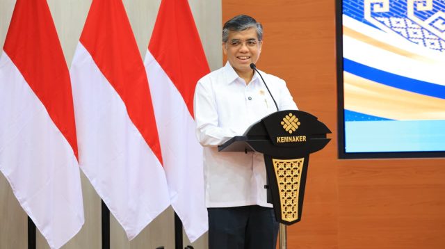 Menteri Ketenagakerjaan Yassierli berbicara di podium Kemnaker dengan latar bendera Indonesia.