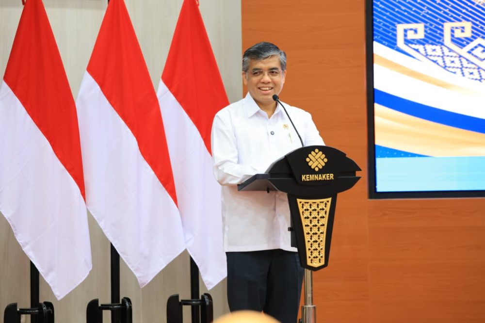 Menteri Ketenagakerjaan Yassierli berbicara di podium Kemnaker dengan latar bendera Indonesia.