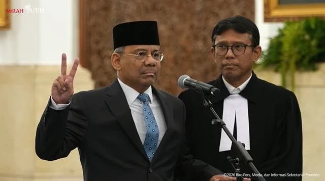Seorang pejabat Suahasil Nazara mengenakan jas dan peci hitam mengangkat dua jari saat pelantikan di Istana Negara, didampingi seorang pejabat lain. Ia adalah Menkeu baru pengganti Purbaya