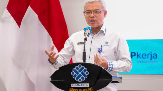 Sekretaris Jenderal Kemnaker Cris Kuntadi berbicara di podium dalam acara Kementerian Ketenagakerjaan dengan latar bendera Merah Putih