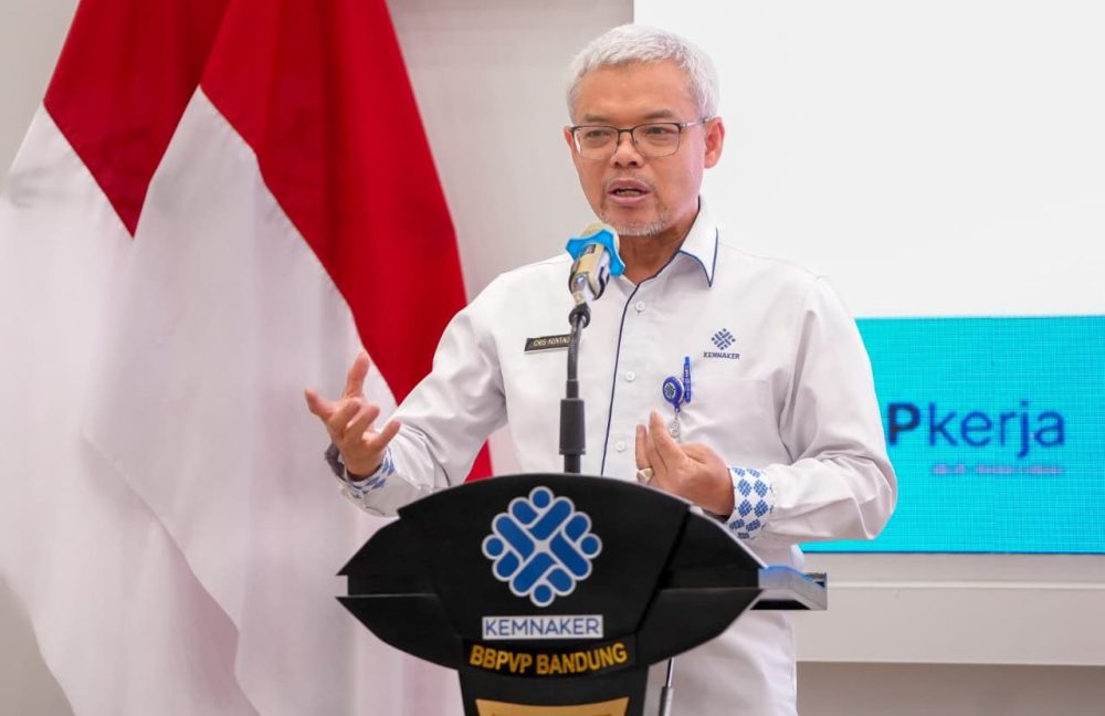 Sekretaris Jenderal Kemnaker Cris Kuntadi berbicara di podium dalam acara Kementerian Ketenagakerjaan dengan latar bendera Merah Putih