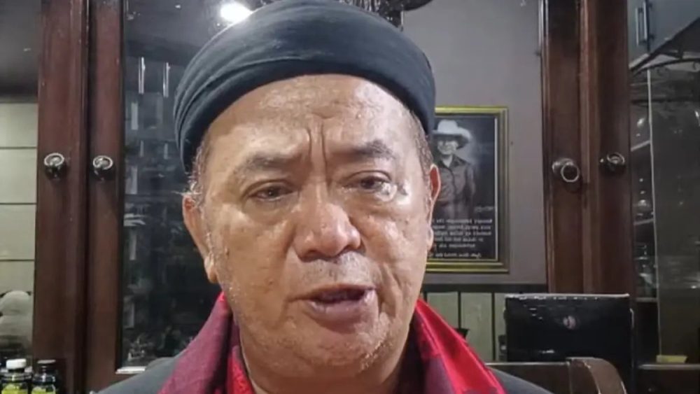Seorang pria mengenakan penutup kepala dan syal merah saat memberikan keterangan terkait polemik dugaan penghinaan terhadap Nabi Muhammad.