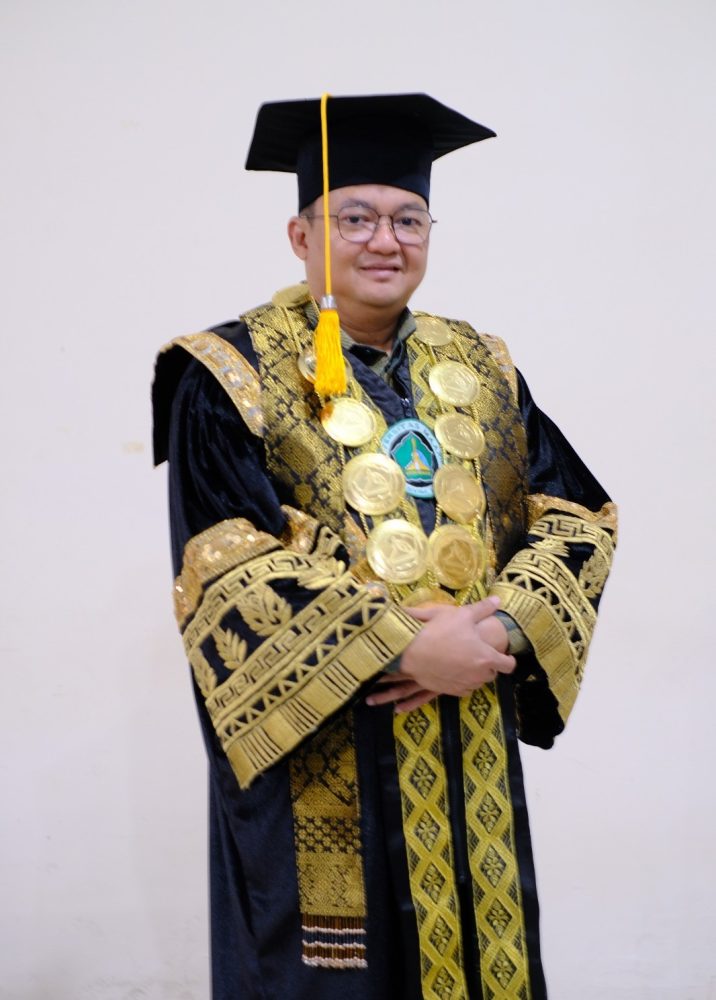 Rektor UMAHA dr. Hidayatullah, Sp.N., mengenakan toga dan busana akademik hitam berornamen emas.