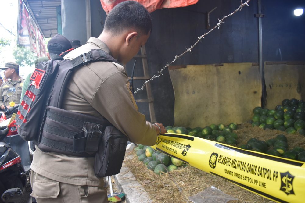 Petugas Satpol PP Surabaya memasang garis segel pada kios buah di kawasan Tambak Mayor–Tanjungsari, Rabu (28/10/2026).