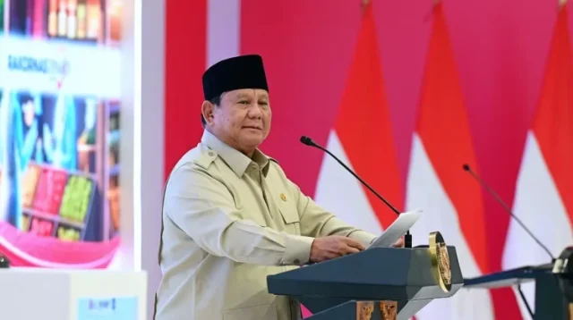 Presiden Prabowo Subianto mengenakan pakaian khaki dan peci hitam saat berpidato di podium berlatar bendera Merah Putih